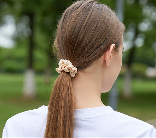 A light - colored 100% silk scrunchie in a woman's hair