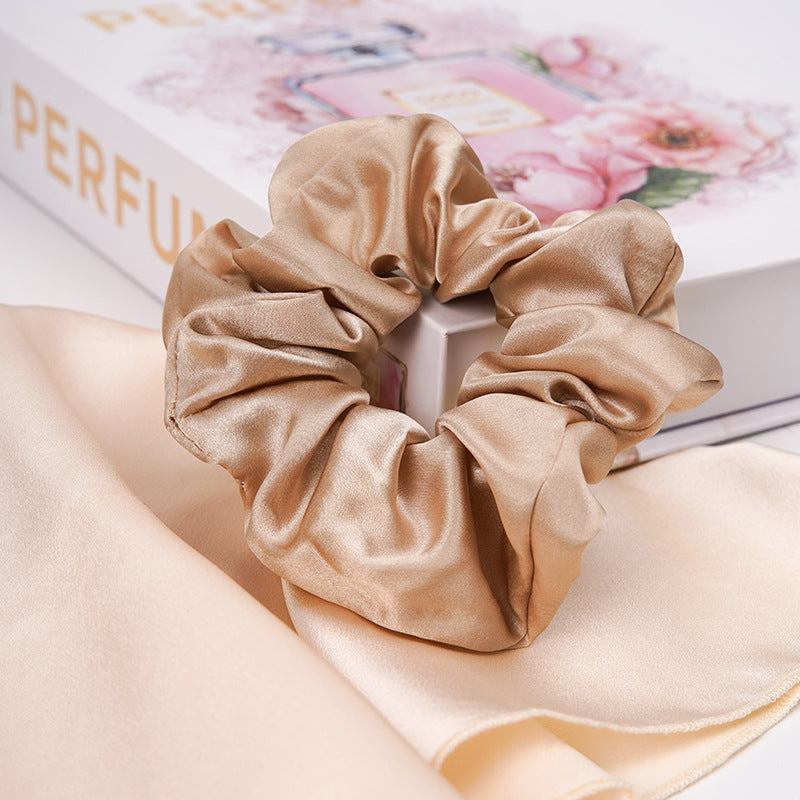 A pastel - pink 100% silk scrunchie worn on a woman's wrist and in her hair-11